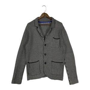 May include: A long-sleeve knit blazer featuring a mix of black and white patterns including houndstooth and vertical stripes. The garment has a notched lapel, three front buttons, one chest pocket, and two lower pockets with black trim.