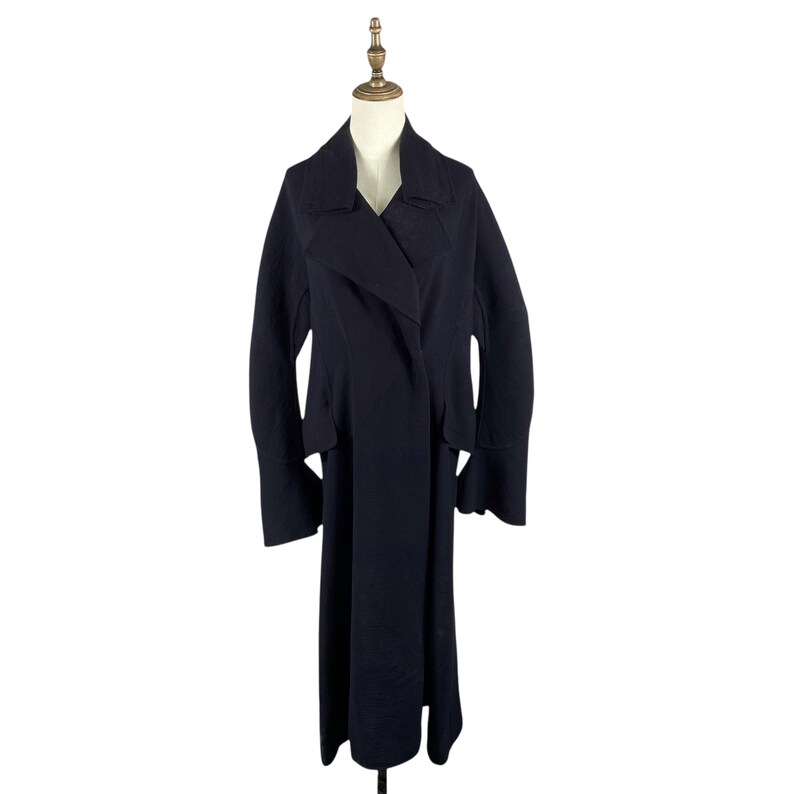 May include: A long, dark navy blue coat with a wide lapel collar and long sleeves. The coat is displayed on a mannequin and has a flowing, floor-length design. The coat's fabric appears to be a medium-weight material.