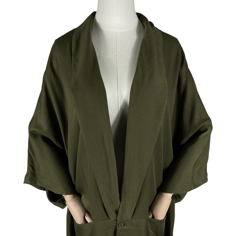 Puede incluir: Bata estilo kimono verde oliva con mangas anchas y corte holgado. La bata tiene dos bolsillos delanteros y un cierre de bot&oacute;n &uacute;nico en la cintura. La tela tiene un brillo sutil.