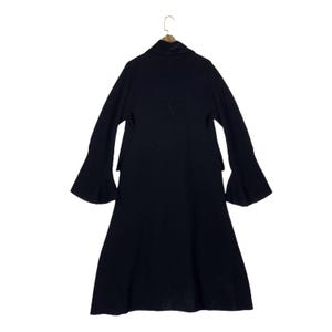 May include: A long, black coat with flared sleeves hangs from a wooden hanger. The coat has a high collar and a long, flowing skirt. The sleeves are wide and bell-shaped, adding a dramatic flair to the garment. The coat is made of a soft, dark fabric.