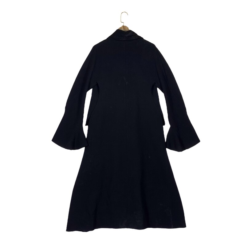 May include: A long, black coat with flared sleeves hangs from a wooden hanger. The coat has a high collar and a long, flowing skirt. The sleeves are wide and bell-shaped, adding a dramatic flair to the garment. The coat is made of a soft, dark fabric.