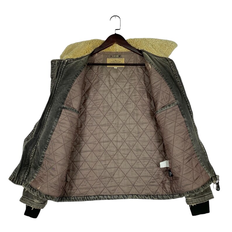 May include: Open denim jacket with a tan faux fur collar and a quilted interior. The jacket is dark grey with black cuffs and a zip closure. The inside lining is a light brown colour.