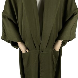 Puede incluir: Bata estilo kimono verde oliva con mangas anchas y cuello chal. La bata tiene dos bolsillos delanteros y un cierre de bot&oacute;n &uacute;nico en la cintura. La tela tiene un brillo sutil, lo que sugiere un material ligero.