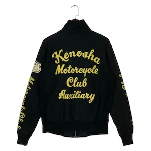 Op de afbeelding: Een zwarte jas met rits en een hoge kraag, voorzien van geel geborduurde tekst op de achterkant met de tekst Kenosha Motorcycle Club Auxiliary. De mouwen hebben ook gele tekst en er zit een klein schildvormig embleem op de rechterschouder.