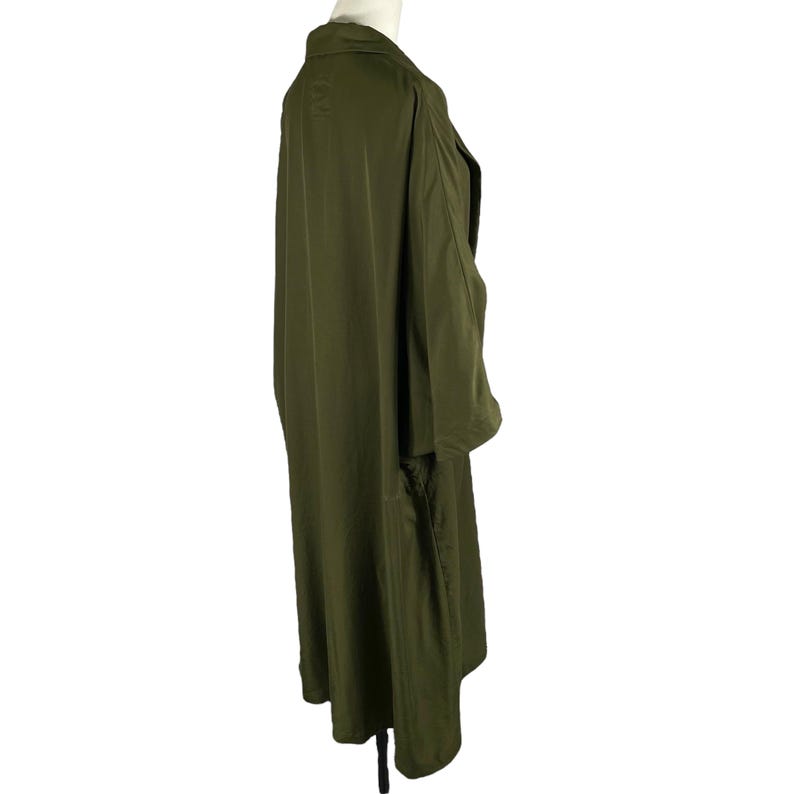 Puede incluir: Gabardina verde oliva con cuello y mangas largas. El abrigo est&aacute; hecho de una tela suave y ligera y tiene un ajuste relajado. El abrigo se exhibe en un maniqu&iacute;.