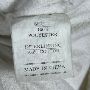 May include: A white fabric tag with black text. The tag reads "SHELL. 100% POLYESTER. INTERLINNING. 100% COTTON. MADE IN CHINA."