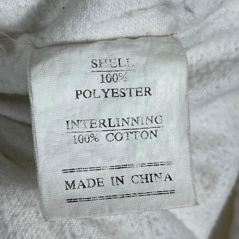 May include: A white fabric tag with black text. The tag reads "SHELL. 100% POLYESTER. INTERLINNING. 100% COTTON. MADE IN CHINA."