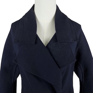 May include: A navy blue coat with a wide lapel and a textured fabric. The coat is displayed on a mannequin, showcasing its tailored design and the details of the collar.