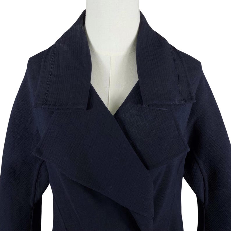 May include: A navy blue coat with a wide lapel and a textured fabric. The coat is displayed on a mannequin, showcasing its tailored design and the details of the collar.
