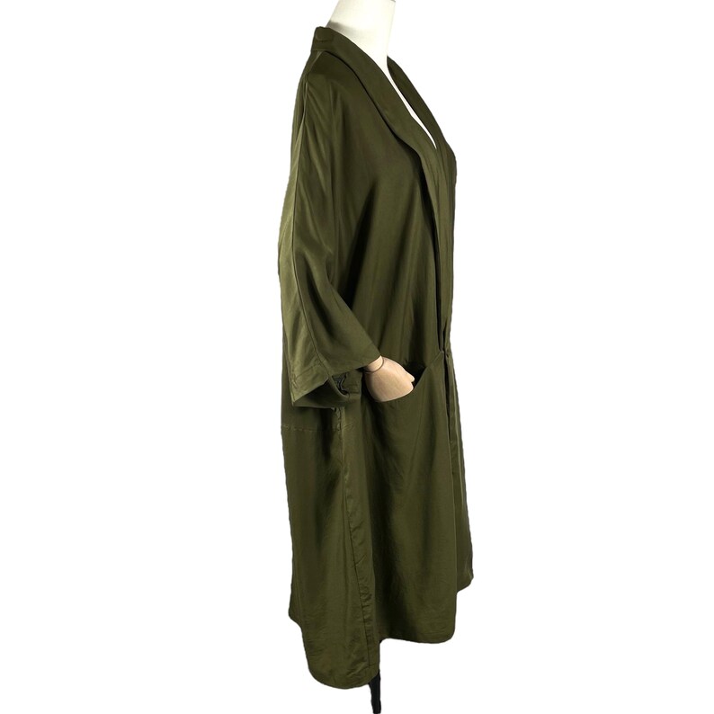 Puede incluir: Abrigo largo verde oliva con cuello chal y dos bolsillos delanteros. El abrigo tiene mangas tres cuartos y un corte holgado. La tela parece ser un material ligero, adecuado para superponer. El abrigo se exhibe en un maniqu&iacute;.