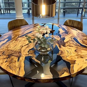May include: A large, round dining table with a unique wood grain pattern and a dark blue resin inlay. The table is surrounded by six chairs with brown backs and cream-colored seats. A glass vase with white flowers sits in the center.