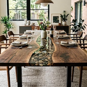 May include: A long dining table featuring two live-edge dark wood slabs joined by a central river of clear resin filled with smooth, multi-colored river stones. The table is supported by black metal legs and surrounded by eight wooden chairs.