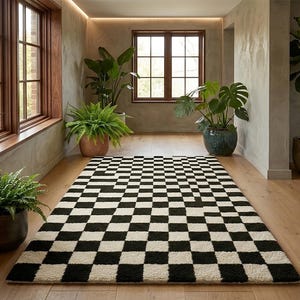 May include: A rectangular area rug featuring a high-contrast black and white checkered pattern. The rug is laid flat on a light-colored wooden floor, displaying a repeating grid of square tiles that cover the entire surface of the floor covering.