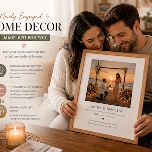 May include: A framed photo with a wooden frame featuring a couple at a beach proposal during sunset. The photo is personalized with the names "James & Sophia" and includes text about their engagement. The image is held by a smiling couple.