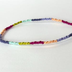 May include: A multi-colored friendship bracelet with a light blue, purple, pink, orange, and green color scheme.