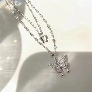 May include: A silver-tone, layered necklace with two butterfly pendants. The larger butterfly pendant is adorned with small, clear crystals. The necklace has a delicate chain design, ideal for adding a touch of elegance to any outfit.