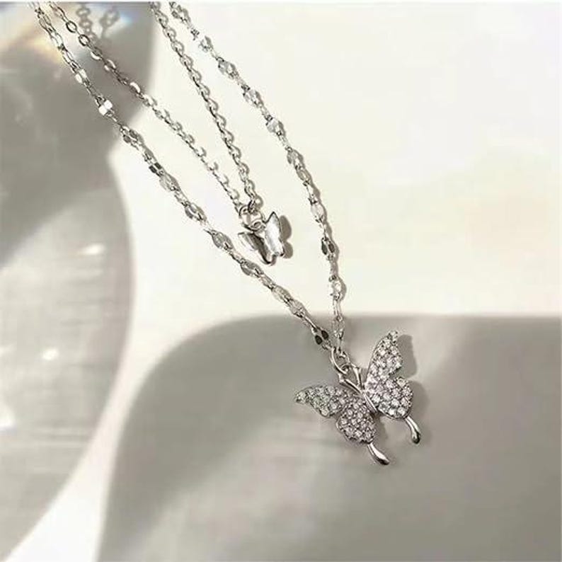May include: A silver-tone, layered necklace with two butterfly pendants. The larger butterfly pendant is adorned with small, clear crystals. The necklace has a delicate chain design, ideal for adding a touch of elegance to any outfit.