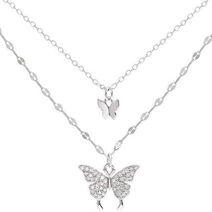 May include: A silver-coloured, layered necklace with two butterfly pendants. The top pendant is a small butterfly, and the lower pendant is a larger butterfly encrusted with small, clear stones. The necklace has two delicate chains.