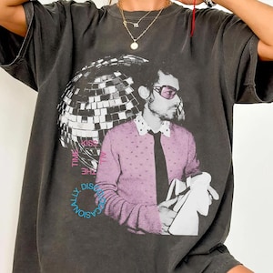 Könnte beinhalten: Dunkelgraues T-Shirt mit einem Aufdruck eines Mannes in einem rosa Pullover und Sonnenbrille, einer Discokugel und dem Text "TIME TO KISS THE DISCO NATIONALLY". Das T-Shirt hat einen Vintage-Look.