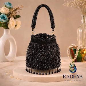 May include: A black beaded handbag with a curved handle and a drawstring closure. The bag is adorned with rows of small beads and a fringe of beads along the bottom. The brand name "RADHYA HANDICRAFTS" is visible at the bottom.