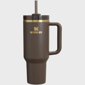 Puede incluir: Un vaso t&eacute;rmico de color marr&oacute;n mate con asa a juego y tapa marr&oacute;n oscuro que incluye una pajita central. El cuerpo muestra el logotipo de Stanley en dorado con un emblema de oso alado. El dise&ntilde;o incluye una banda dorada bajo la tapa.
