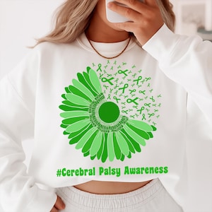 Może przedstawiać: Biała bluza z zielonym kwiatowym wzorem i zielonymi wstążkami. Tekst "#Cerebral Palsy Awareness" jest wydrukowany na zielono. Kwiatowy wzór znajduje się z przodu bluzy.