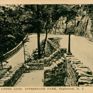 May include: A black and white postcard showing a winding road through a wooded area with stone walls and a sign that reads "Upper Loop, Interstate Park, Englewood, N.J."