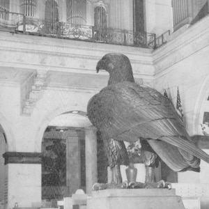 May include: A black and white photograph of a large eagle statue inside a grand hall. The eagle is perched on a stone pedestal. The text at the bottom reads "THE EAGLE, The Grand Court, John Wanamaker, Philadelphia."
