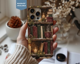 Puede incluir: Una funda para smartphone con una ilustración impresa de estanterías de madera llenas de libros, ramas de pino, piñas y velas encendidas. Una taza humeante descansa en un estante. La funda tiene un recorte para una cámara de triple lente y una etiqueta azul que dice MAGSAFE AVAILABLE.