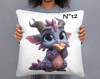 May include: White throw pillow featuring a cartoon dragon eating pizza. The dragon is purple, pink, and blue with large eyes. The pillow has the number 12 in black on the upper right corner.