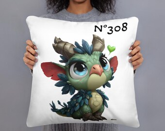 May include: White square pillow featuring a cartoon dragon with large blue eyes, green and blue feathers, and red ears. The dragon is sitting on the pillow. The text "N°308" and a green heart are above the dragon.