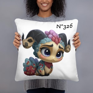 Può includere: Cuscino quadrato bianco con una creatura dei cartoni animati colorata con grandi occhi blu, corna e una coda di piume. Il cuscino ha il numero "N°326" stampato in nero.