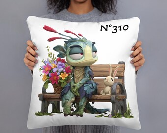 May include: White square pillow featuring a whimsical illustration of a creature and a rabbit on a park bench. The creature has blue and green feathers, and is holding a basket of colorful flowers. The text "N°310" is printed on the pillow.