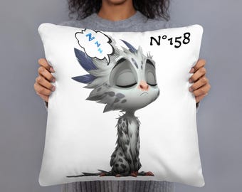 May include: White square pillow featuring a cartoon illustration of a sleepy creature with closed eyes, gray and white spotted fur, and blue feather accents. A speech bubble with 'Zzz' is above the creature's head, and the number 'No. 158' is printed on the pillow.