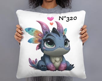 May include: White throw pillow featuring a cartoon dragon illustration. The dragon is blue with colorful wings and accents, and large green eyes. The pillow has the text "N°320" and two hearts.