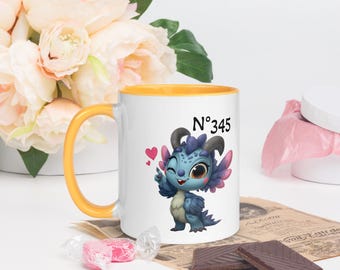 May include: White ceramic mug with a yellow handle and interior. The mug features a cartoon dragon illustration with the number "N°345". The dragon is blue with purple wings and is winking. Two pink hearts are next to the dragon.