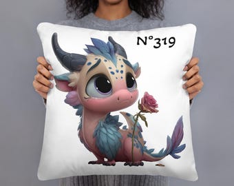 May include: White square pillow featuring a cartoon dragon with pink, blue, and gray tones, holding a pink rose. The dragon has large eyes and a sad expression. The text "N°319" is printed in black.