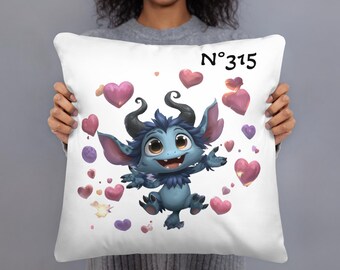 May include: White throw pillow featuring a cartoon blue creature with horns, large ears, and a smiling expression. The pillow is decorated with pink and purple hearts and the text "N° 315".