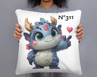 May include: White square pillow featuring a cartoon monster with blue fur, large green eyes, and small horns. The monster is giving a peace sign. The pillow has the text "N°311" and two pink hearts.