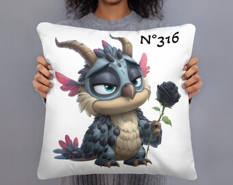 May include: White throw pillow featuring a cartoon dragon holding a black rose. The dragon has blue and gray feathers, brown horns, and teal eyes. The pillow has the number "N°316" printed in black.