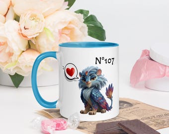May include: White ceramic mug with a blue interior and handle. The mug features a cartoon illustration of a blue and purple creature with a heart speech bubble and the number "107".