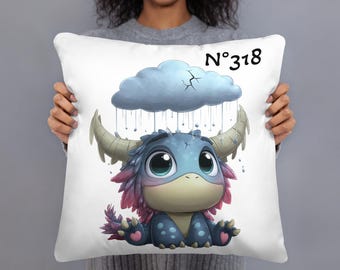 May include: White decorative pillow featuring a cartoon monster with big eyes, horns, and a cloud overhead. The monster is blue, pink, and purple. The pillow has the text "N°318" in black.