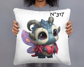 May include: White decorative pillow featuring a cartoon dragon-like creature with large eyes, holding a broken heart. The creature has blue, gray, and red coloring, with purple wings. The pillow has the number "317" printed on it.