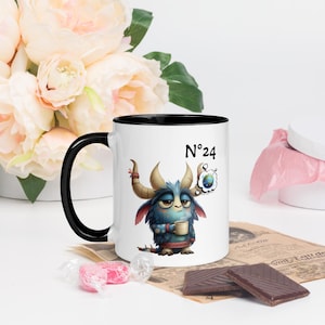 Pode incluir: Caneca de cerâmica branca com interior e alça pretos, com um monstro de desenho animado segurando uma xícara. A caneca tem o número "24" impresso. O monstro é azul, com chifres e um balão de pensamento.