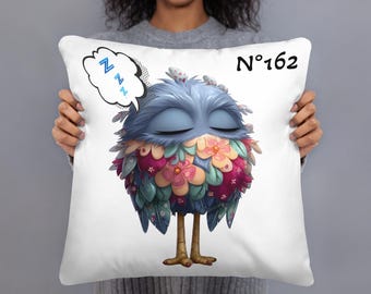 May include: White square pillow featuring a cartoon bird with closed eyes, blue feathers, and colorful floral accents. The pillow has the number "162" printed on it, and a speech bubble with "Z"s. A decorative item.