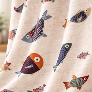 Könnte beinhalten: Cremefarbener Stoff mit einem allover Muster aus gestickten Fischen in verschiedenen Farben. Die Fischdesigns umfassen Blau-, Rot-, Orange- und Grüntöne mit detaillierten Mustern und Augenakzenten. Der Stoff scheint ein Vorhang oder ein ähnliches Textil zu sein.