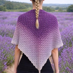 May include: A purple and white ombre crochet shawl. The shawl is draped over the shoulders. The background is a field of lavender flowers.