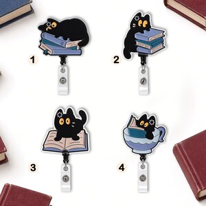 May include: Four retractable badge reels featuring black cats with large yellow eyes. Design 1 shows a cat on a stack of books, 2 shows a cat climbing books, 3 shows a cat on an open book, and 4 shows a cat reading inside a blue teacup.