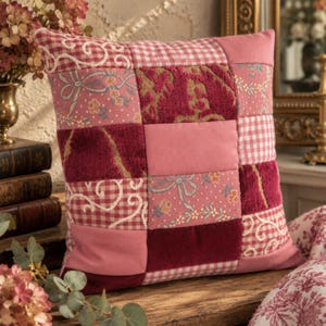 May include: A square throw pillow featuring a patchwork design of various pink and burgundy fabrics. The pattern includes sections of gingham check, floral prints with white ribbons, solid pink panels, and textured deep red velvet squares.