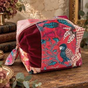 Può includere: Una trousse patchwork che combina velluto rosso, tessuto a quadretti vichy rosso e bianco e un vivace tessuto rosso stampato con foglie verde acqua e un gufo blu. La trousse presenta una chiusura a zip dorata con una linguetta in tessuto.